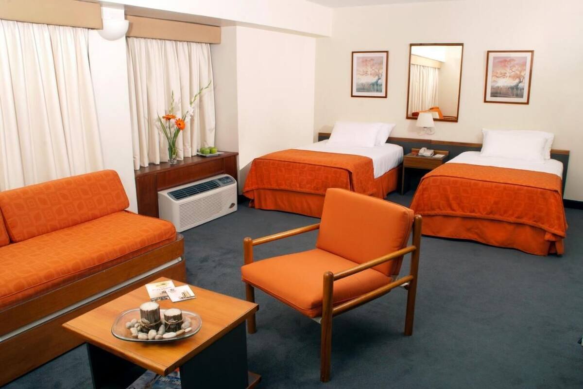 A hotel room with two beds, a sofa, a chair, a small table with a tray of items, and a heater.