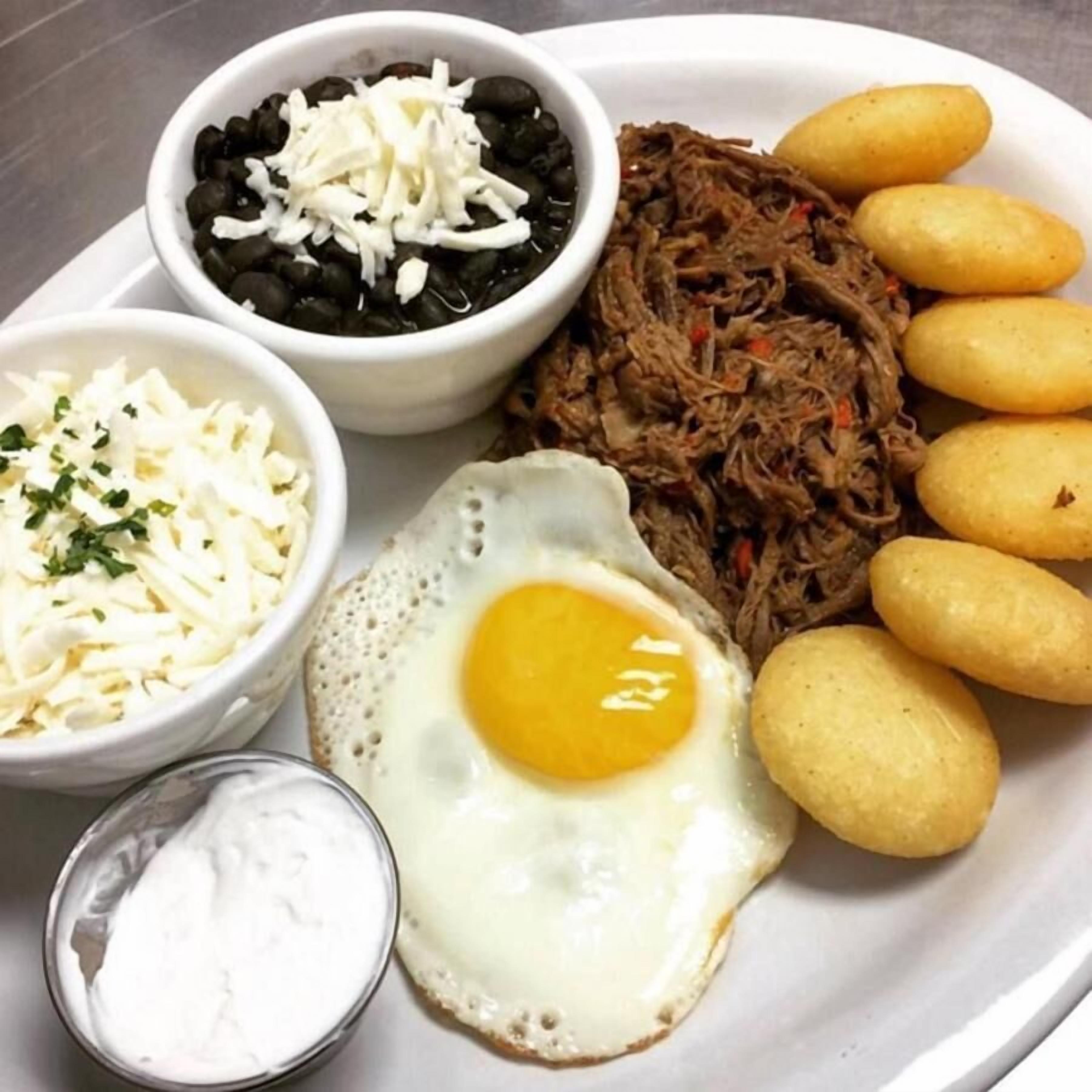 Une assiette garnie de fromage râpé, de haricots noirs, de viande effilochée, d’un œuf au plat et de chips de bananes plantains.
