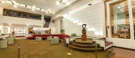 A spacious lobby with a central seating area, a staircase, and a large window with a view.