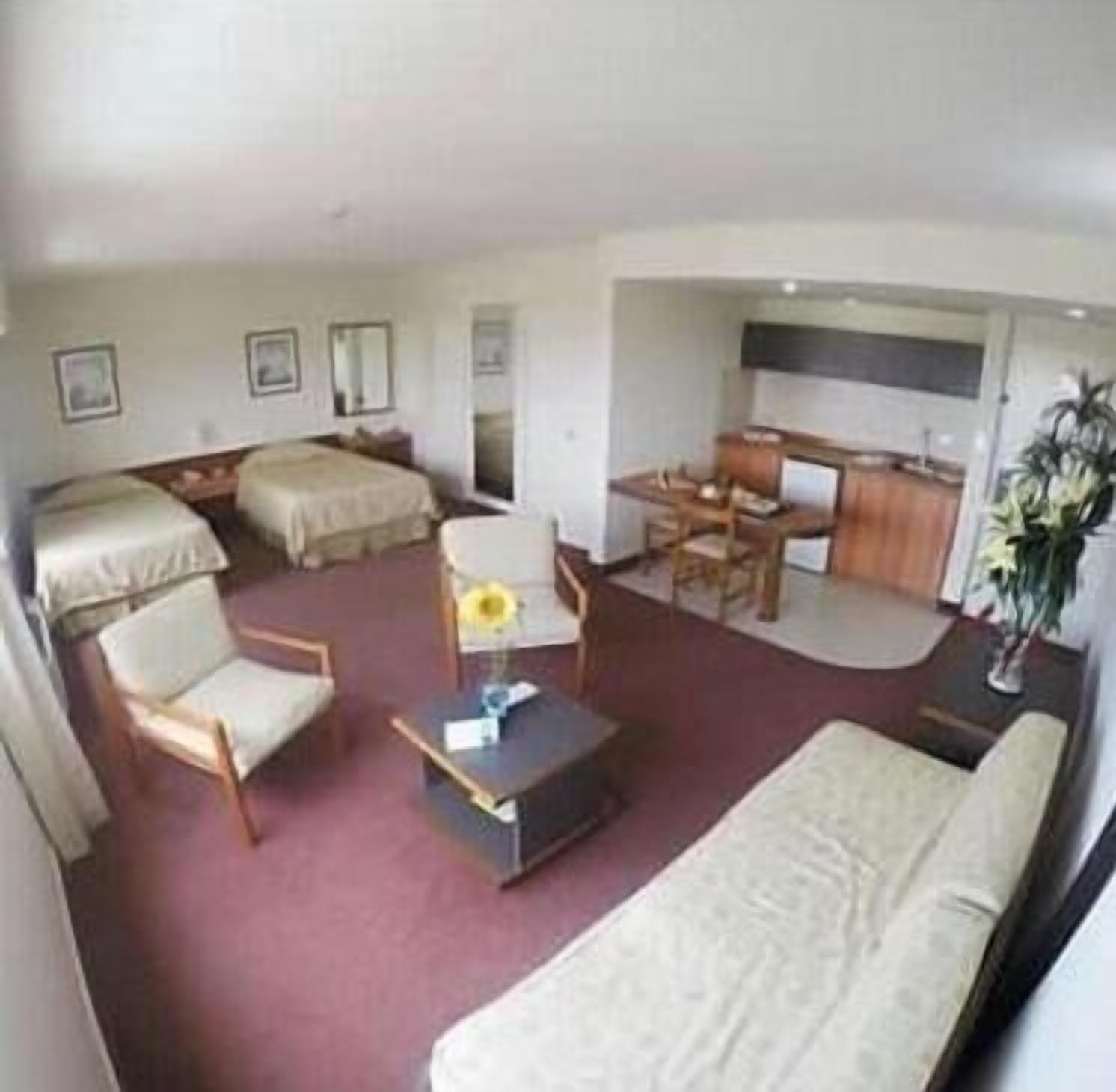 A hotel room with a bed, a desk, a chair, a sofa, and a small table with a vase of flowers.