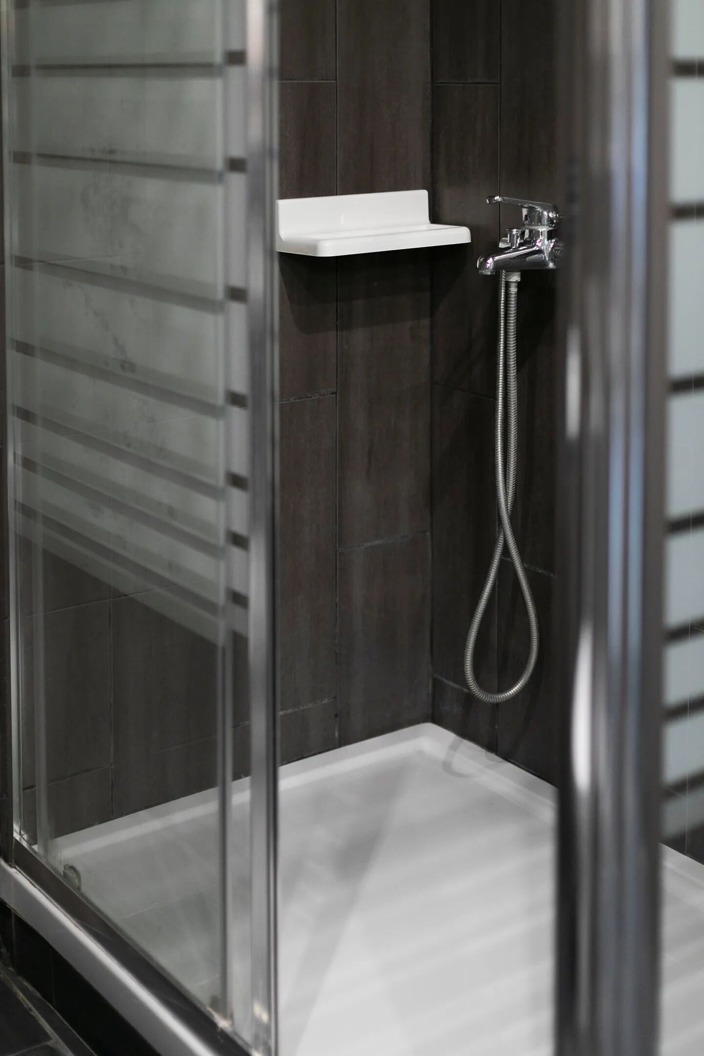 A modern shower enclosure with a glass door, a chrome showerhead, and a white shelf.