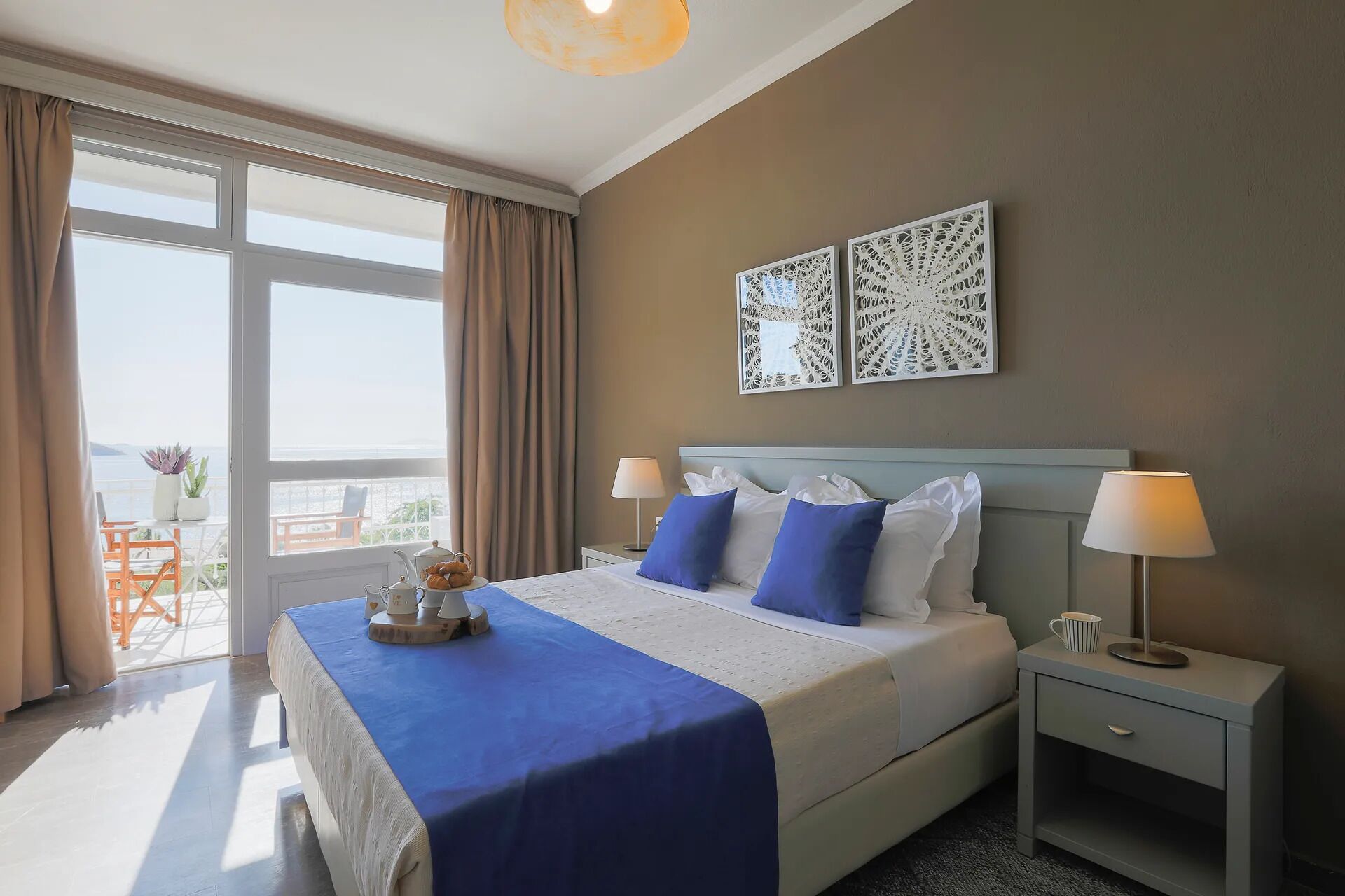 A hotel room with a bed, two bedside tables, a window with curtains, and a balcony with a view.