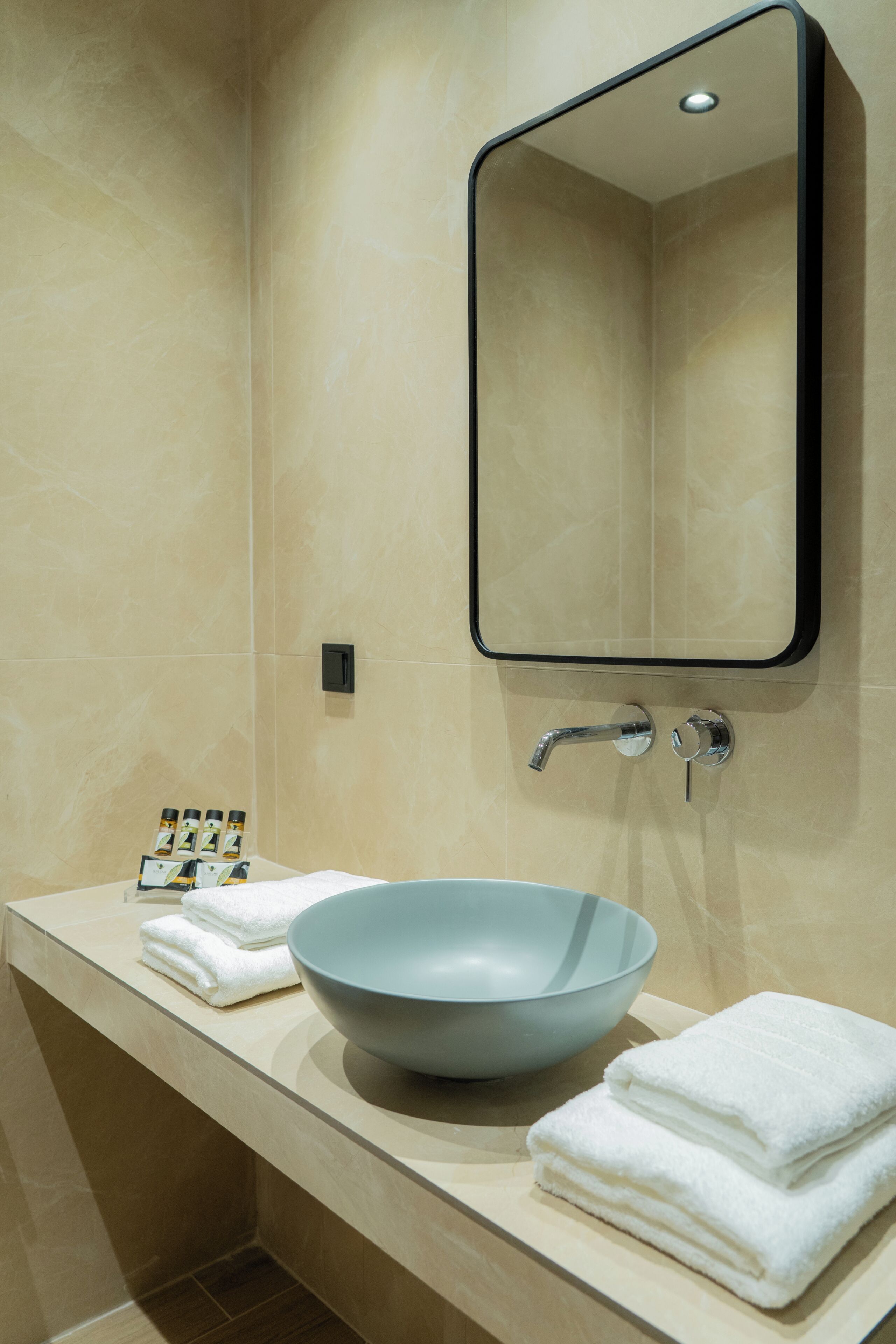 A bathroom with a beige tiled wall, a large mirror, a sink with a blue basin, and neatly folded white towels.