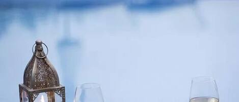 A table with a candle, two glasses of white wine, and a plate of food by a poolside.