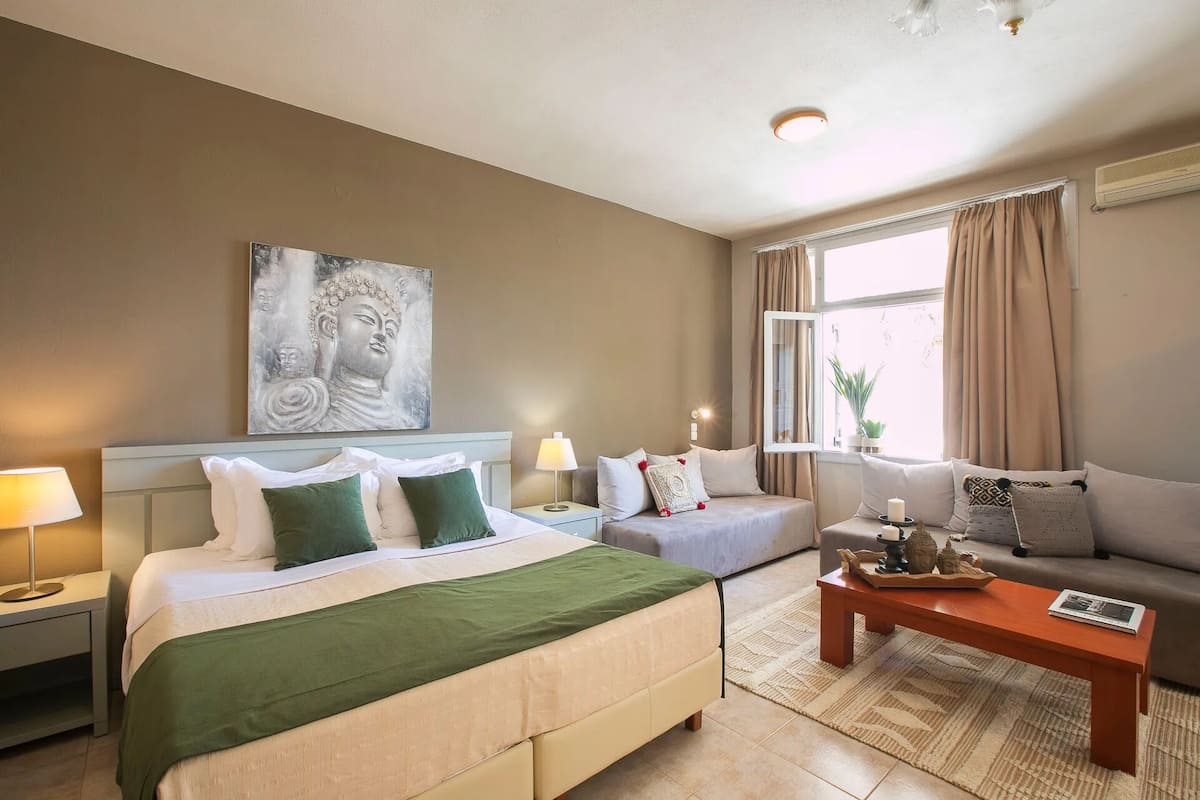 Una habitación de hotel con una cama, un sofá, una mesa de centro y un ventanal con cortinas.