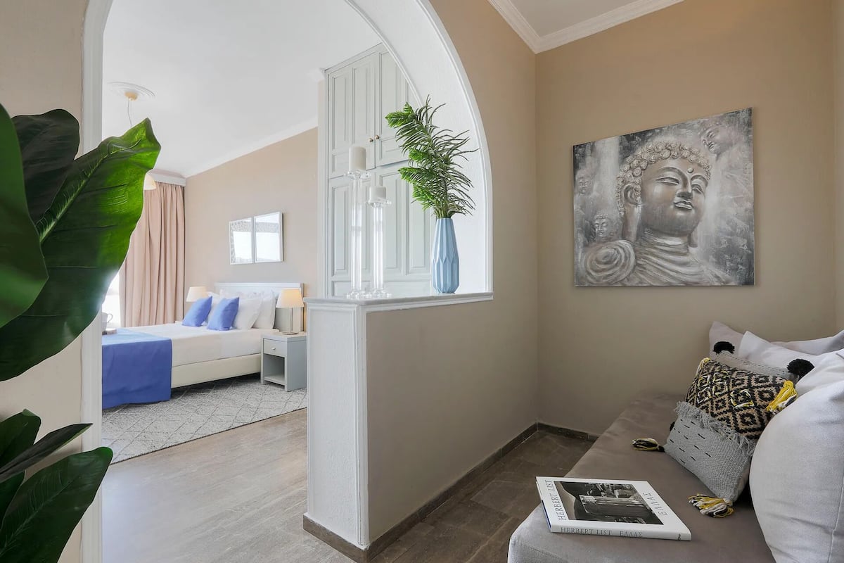 Una sala de estar moderna con un sofá, un sillón de lectura, un ventanal con una planta y un cuadro de Buda.