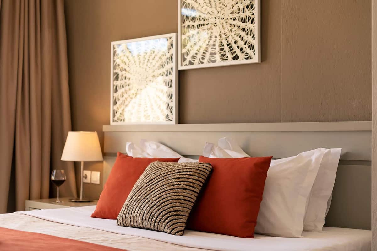 Habitación de hotel con una cama, almohadas rojas y blancas, una lámpara y dos obras de arte en la pared.