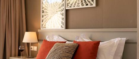 A hotel room with a bed, red and white pillows, a lamp, and two wall art pieces.