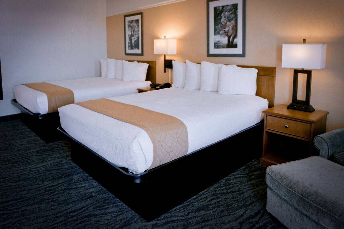 A hotel room with two beds, a nightstand, a lamp, and a chair.