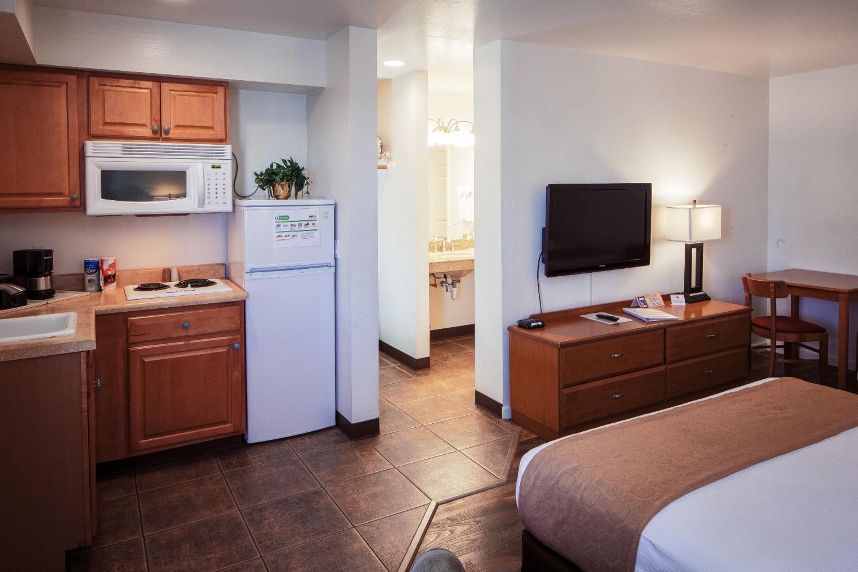 Habitación de hotel con kitchenette, cama, televisor y escritorio con silla.