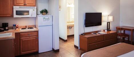 Habitación de hotel con kitchenette, cama, televisor y escritorio con silla.