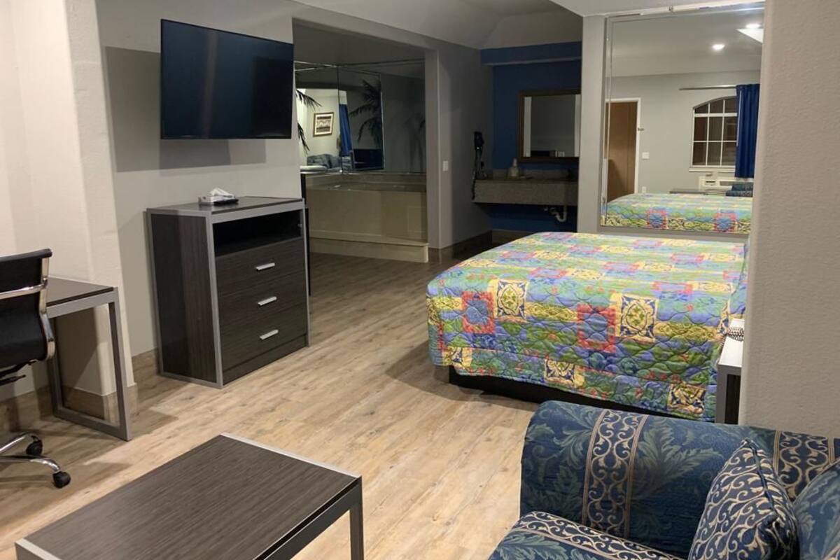A hotel room with a bed, a desk, a chair, a mirror, and a television.