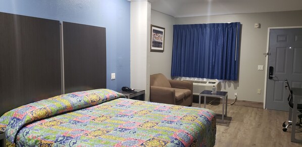 A hotel room with two beds, a chair, a desk, a window with curtains, and a door.