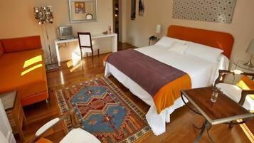 A hotel room with a bed, a desk, a chair, a sofa, and a rug.
