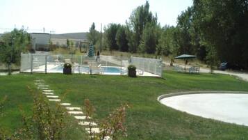 A backyard with a swimming pool, a fenced area, and a grassy lawn.
