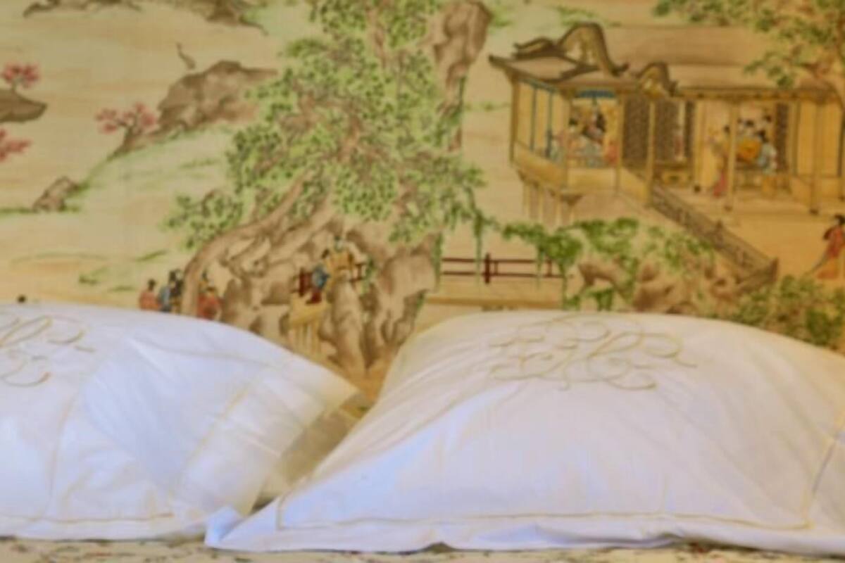 Un lit avec des oreillers blancs et une fresque représentant une scène traditionnelle avec des personnes et un bâtiment.