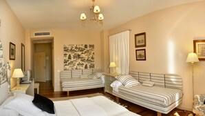 Habitación de hotel con una cama, dos sofás, un escritorio con lámpara, una silla y un cuadro en la pared.