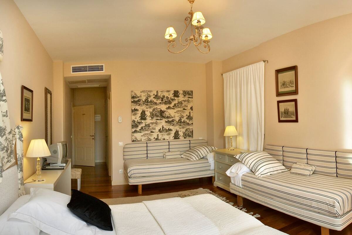 Une chambre d’hôtel avec un lit, deux canapés, un bureau avec une lampe, une chaise et un tableau au mur.