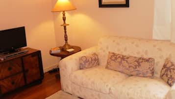 A living room with a sofa, a TV on a wooden cabinet, a lamp, and a framed picture on the wall.