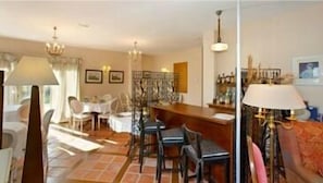 Un comedor con una mesa de madera, sillas y una barra. Hay sillas alrededor de la mesa y una araña cuelga del techo.