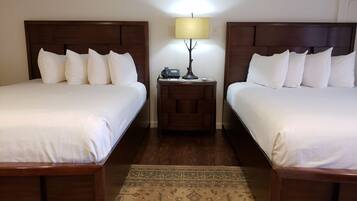 Una habitación de hotel con dos camas individuales, una mesita de noche con lámpara y una alfombra estampada.