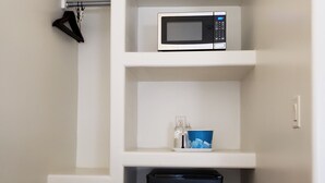 A compact kitchenette with a microwave, a small refrigerator, and a trash bin. - The Iron Horse Inn (Cottonwood)