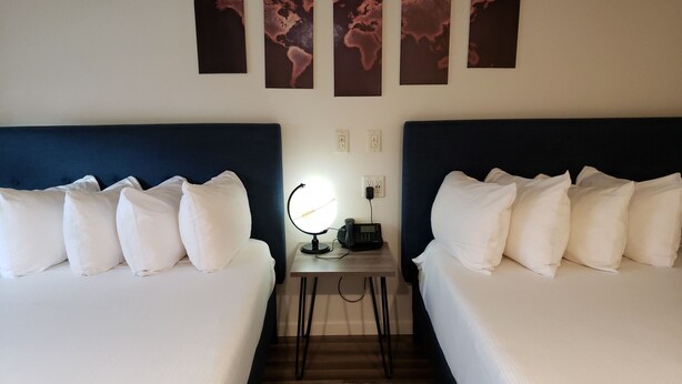 A hotel room with two beds, a nightstand with a phone and a lamp, and three world maps on the wall. - The Iron Horse Inn (Cottonwood)