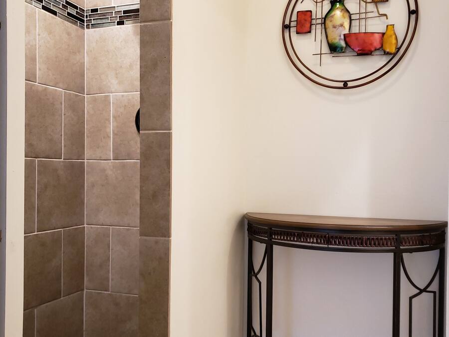 A bathroom with a shower area, a decorative wall piece, and a small table.
