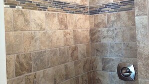 A shower with beige tiles and a metal showerhead. - The Iron Horse Inn (Cottonwood)