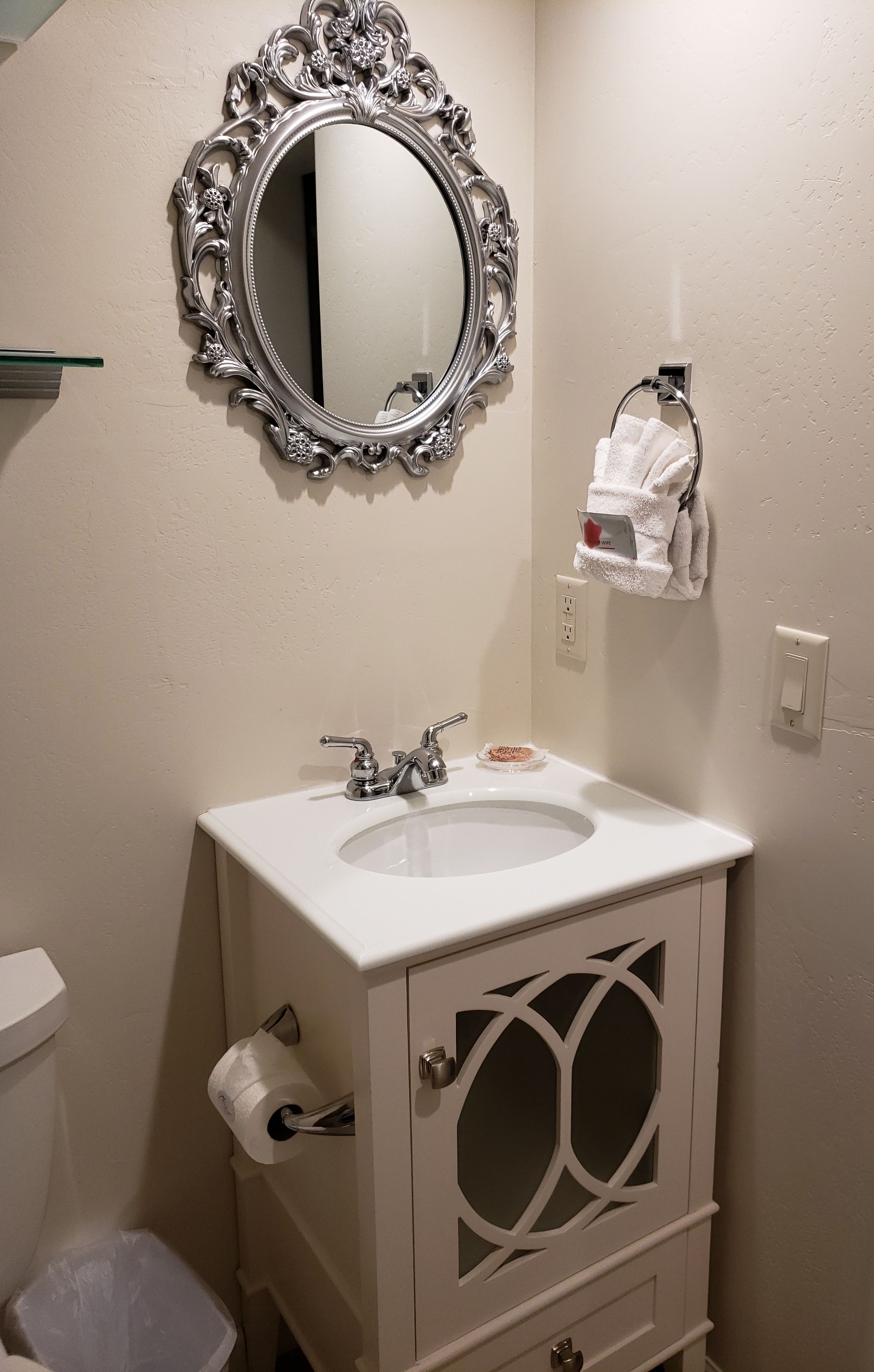 A bathroom with a white sink, a mirror with an ornate frame, a towel rack, and a toilet paper holder.