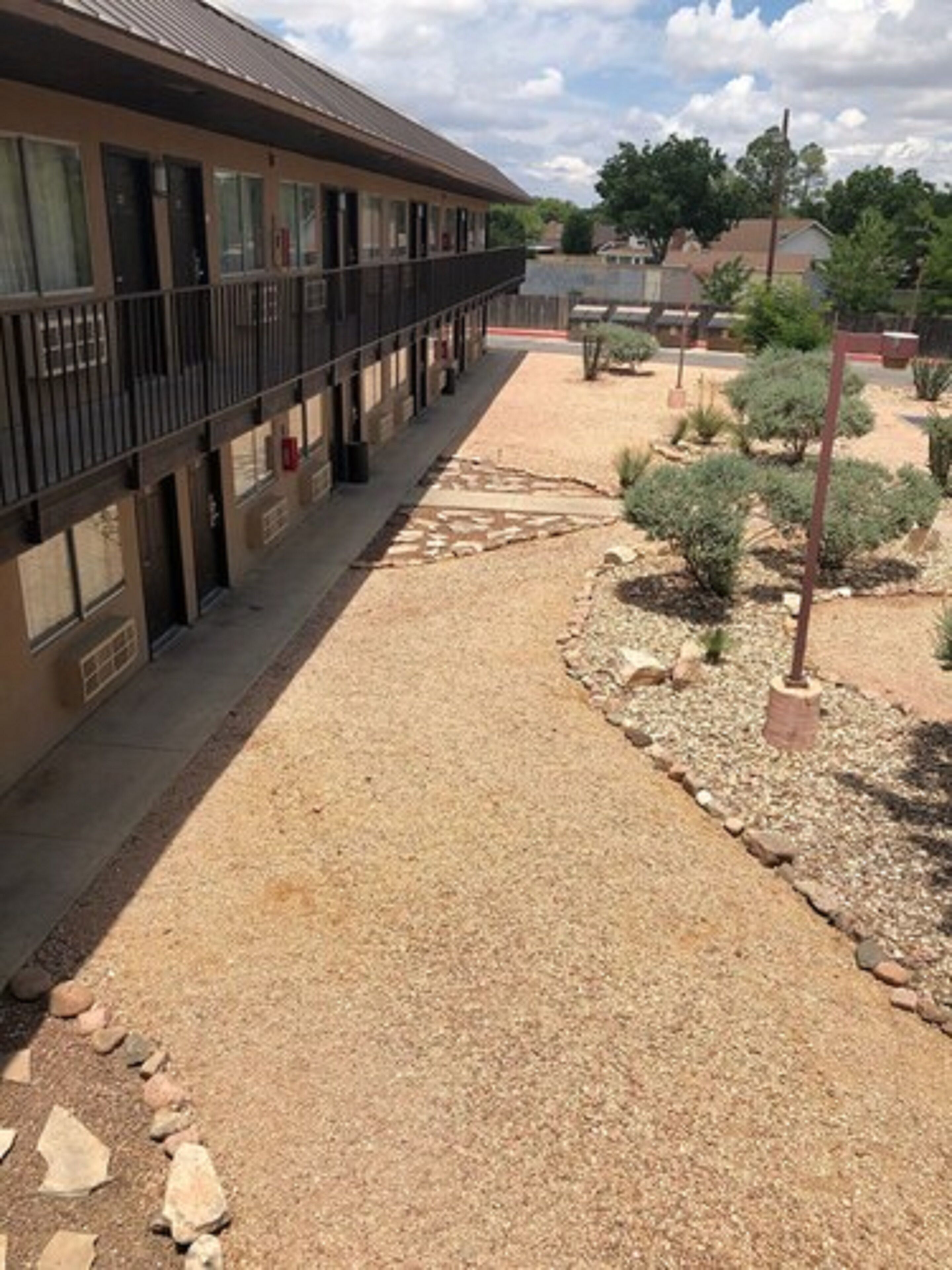 Un hôtel doté d’un espace extérieur couvert, d’un chemin de gravier et de parterres de jardin aménagés.