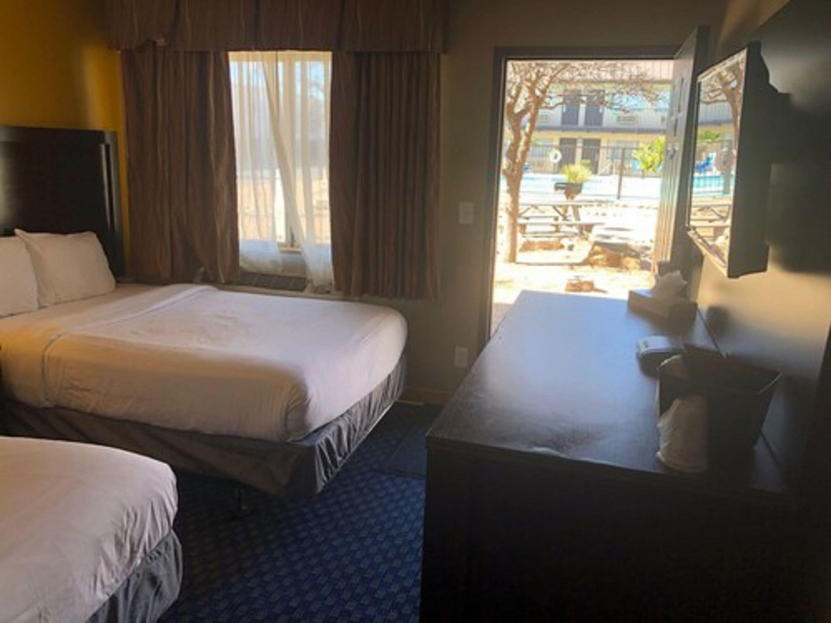 A hotel room with two beds, a desk, and a window with curtains.