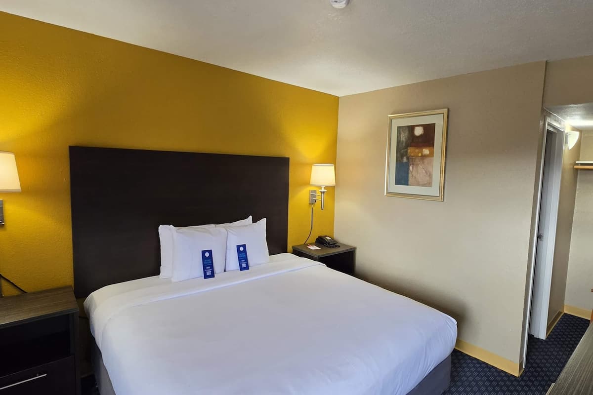 A hotel room with a large bed, two bedside lamps, a nightstand with a phone, and a door to the right.