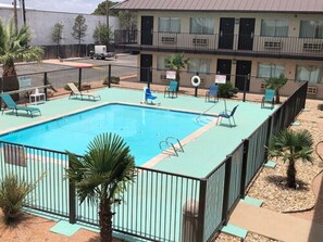 A rectangular pool with a surrounding fence, lounge chairs, and palm trees.