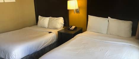 Ein Hotelzimmer mit zwei Einzelbetten, jeweils mit weißer Bettwäsche, einem Nachttisch mit Lampe und einem Telefon.