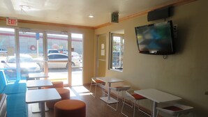 A restaurant interior with tables and chairs, an exit sign, and a TV mounted on the wall.