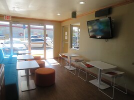 Interior de restaurante con mesas y sillas, una señal de salida y un televisor en la pared.