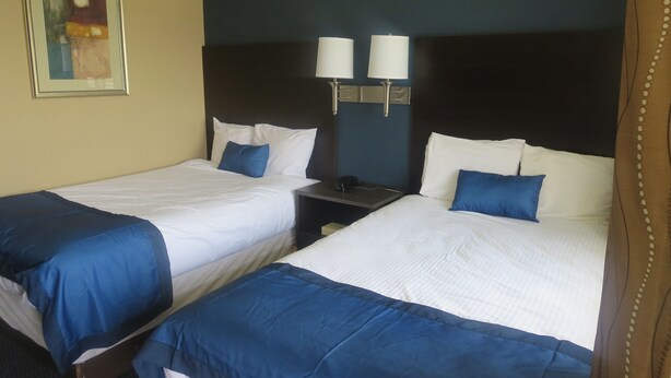 Two single beds with white and blue bedding, a nightstand with a lamp, and a painting on the wall.