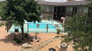 A pool area with a sandy ground, a tree, and a building in the background.