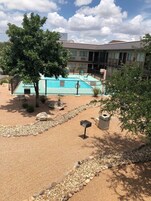 Zona de piscina con suelo de arena, un árbol y un edificio al fondo.