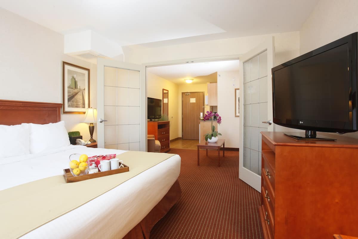 Habitación de hotel con cama, televisión, escritorio y baño visible a través de una puerta abierta.