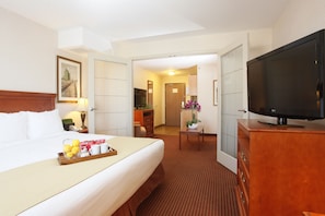 A hotel room with a bed, a TV, a desk, and a bathroom visible through an open door.