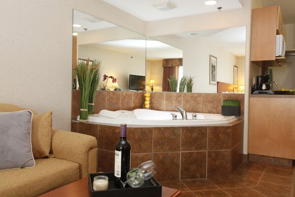 Une salle de bain moderne avec une grande baignoire, un lavabo et un miroir. Un canapé avec des coussins se trouve dans le salon attenant.