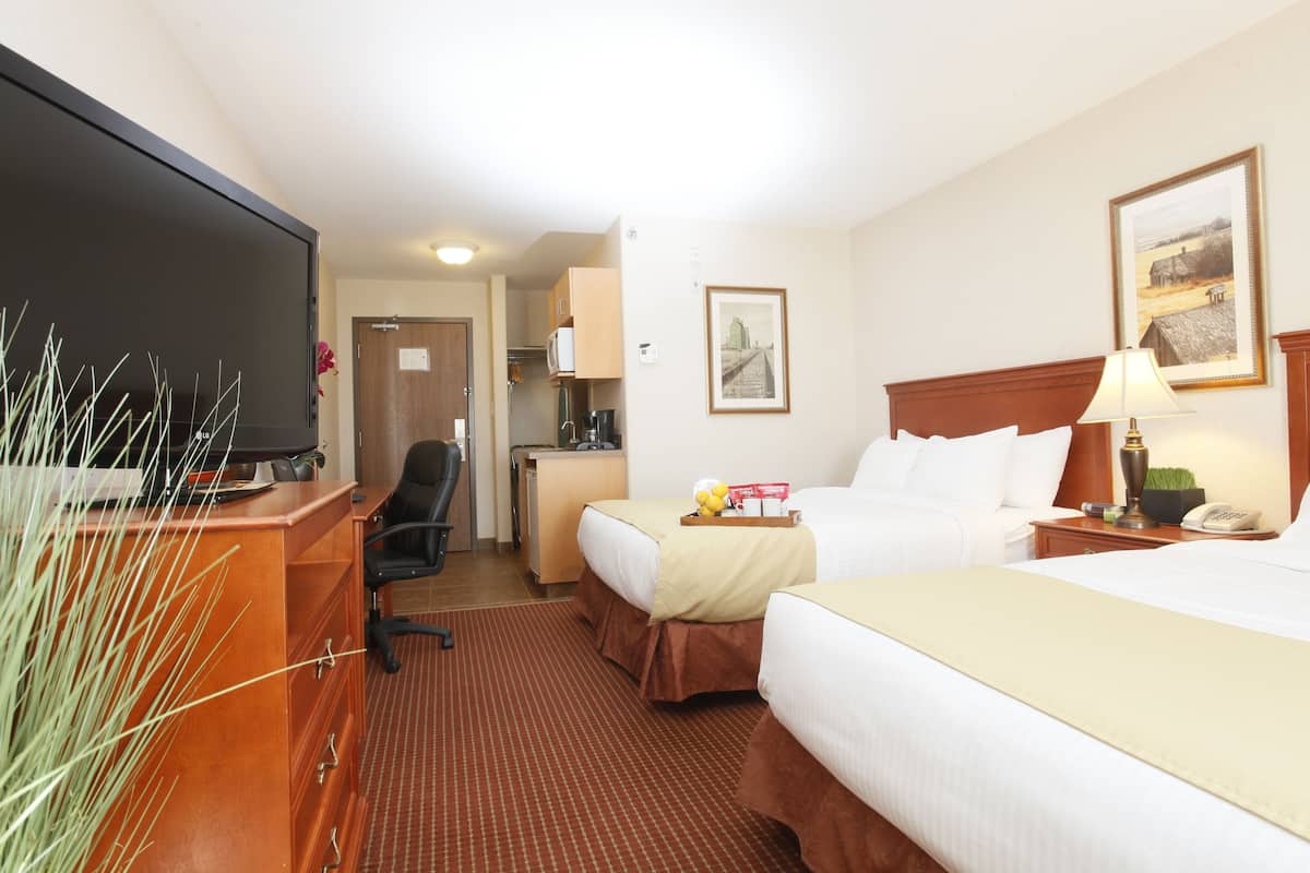 Habitación de hotel con dos camas, un escritorio con computadora, un televisor y una kitchenette pequeña.