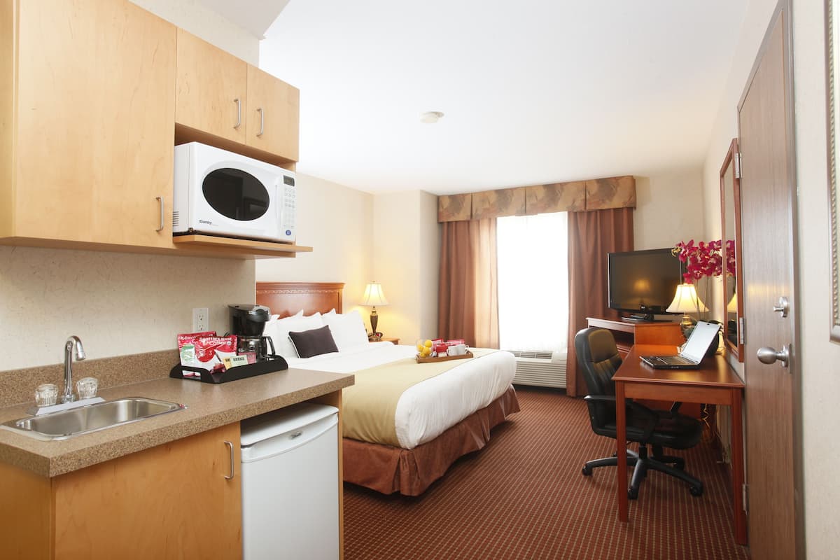 Habitación de hotel con cama, escritorio, silla, microondas, lavamanos y televisión.