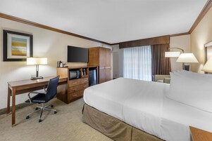 Una habitación de hotel con una cama grande, un escritorio con una silla, un televisor y una ventana con cortinas.
