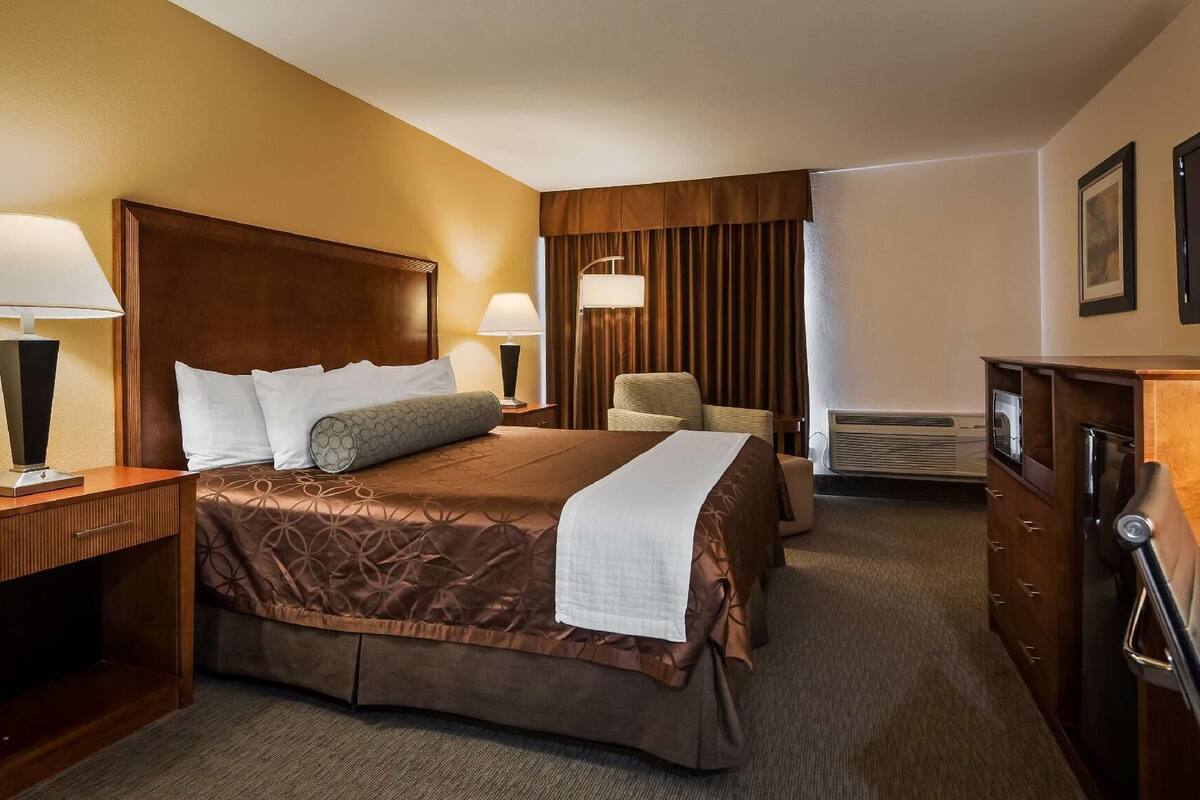 A hotel room with a large bed, two bedside tables with lamps, a chair, a television, and a dresser.