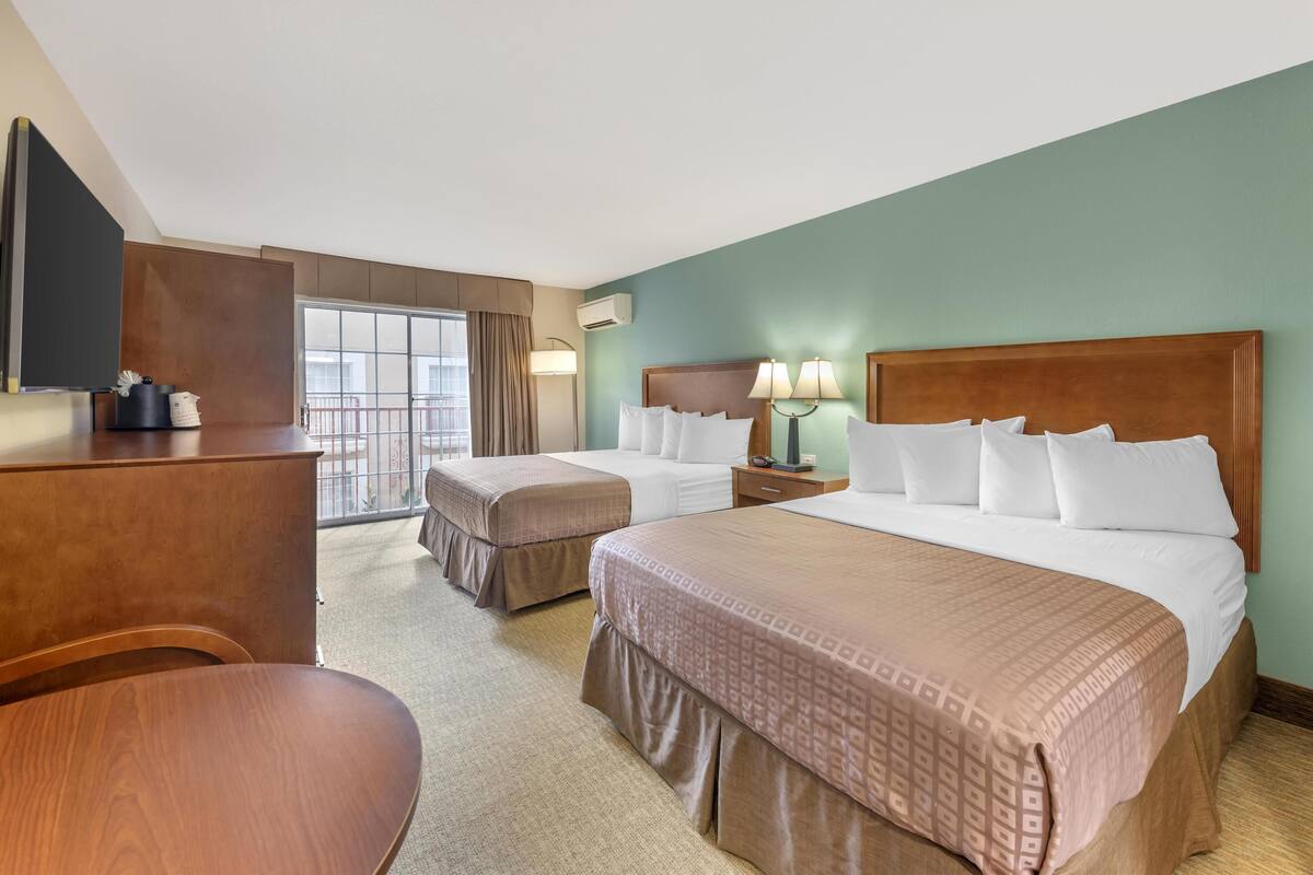 A hotel room with two beds, a desk, a chair, and a television.
