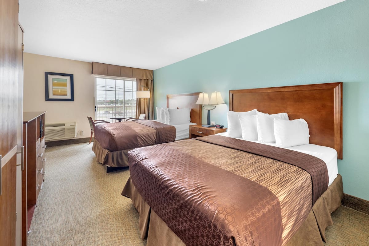 A hotel room with two beds, a desk, a chair, and a window with curtains.