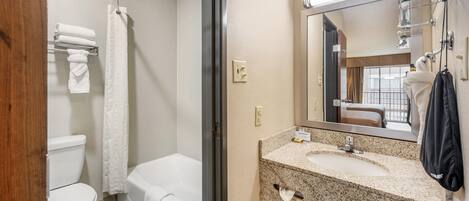Un baño con inodoro, bañera y lavamanos con espejo.